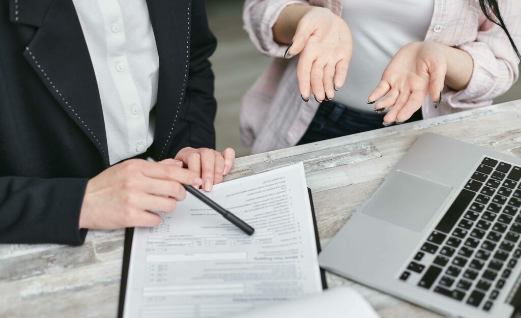 Two professionals discussing a contract at a business meeting with documents and a laptop.